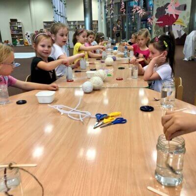 Dzieci siedzące przy stole wykonują eksperyment. Mieszają łyżeczkami w szklanych słoikach wypełnionych wodą i solą. Kliknięcie powoduje powiększenie zdjęcia.