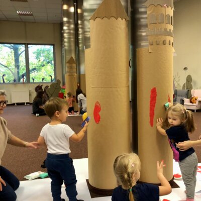 Trójka dzieci odbija za pomocą gąbki, czerwone cegiełki na papierowych zamkach. Kliknięcie powoduje powiększenie zdjęcia.