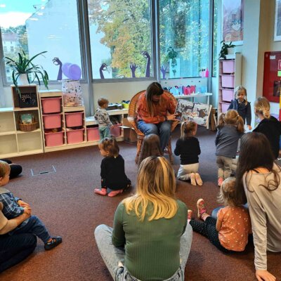 Dzieci siedzą wraz z rodzicami i uważnie słuchają książki czytanej przez Panią Bibliotekarkę. kliknięcie powoduje powiększenie zdjęcia.