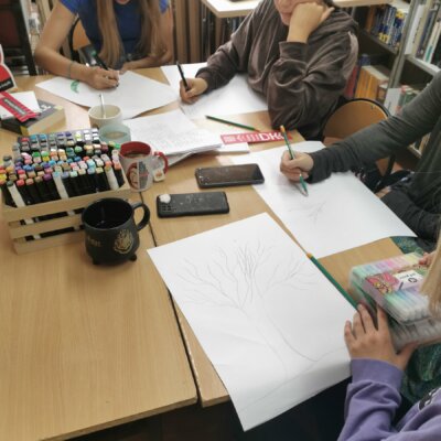 Cztery osoby siedzą przy stole i rysują na kartkach papieru. Kliknięcie powoduje powiększenie zdjęcia.