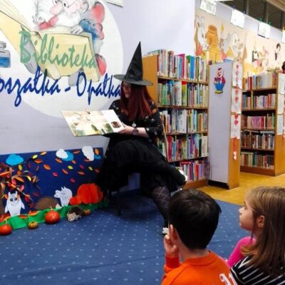 Bibliotekarka w przebraniu czarownicy czyta dzieciom bajkę. Kliknięcie powoduje powiększenie zdjęcia.