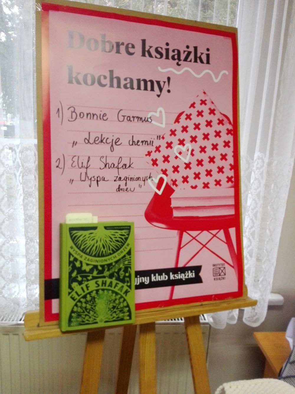 Plakat DKK i książka Elif Shafak „Wyspa zaginionych drzew” na sztaludze.