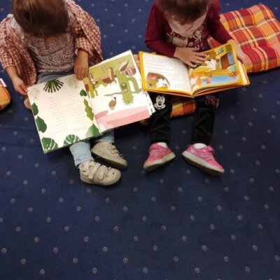 Dwie dziewczynki siedzą na dywanie i przeglągają książki. Klikniecie powoduje powiększenie zdjęcia.