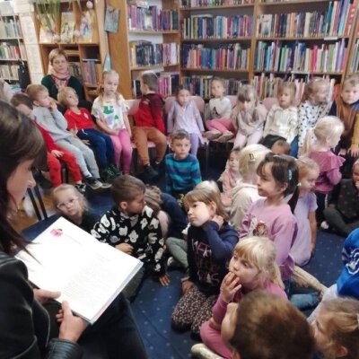 Liczna grupa dzieci słucha bajki czytanej przez kobietę. Kliknięcie powoduje powiększenie zdjęcia.
