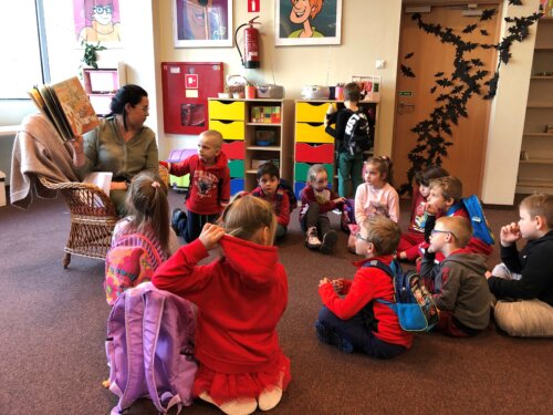 Dzieci siedzą w okręgu i słuchają czytanej im książki.