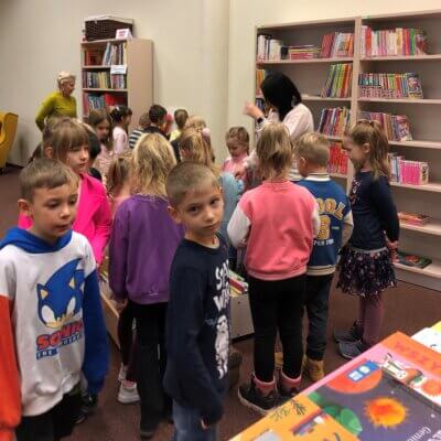 Uczestnicy lekcji bibliotecznej słuchają uważnie Pani Bibliotekarki, która oprowadza ich po Oddziale Dziecięcym.