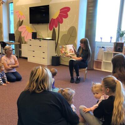 Dzieci wraz z opiekunami słuchają książki czytanej przez Panią bibliotekarkę. Kliknięcie powoduje powiększenie zdjęcia.