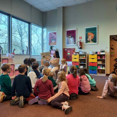 Dzieci siedząc w okręgu słuchają książki czytanej przez Panią bibliotekarkę. Kliknięcie powoduje powiększenie zdjęcia.