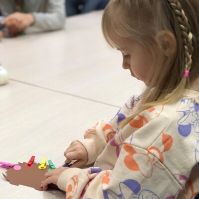 Dziewczynka przyczepia kolorowe klamerki do odpowiednich barw na wyciętym jeżyku. Kliknięcie powoduje powiększenie zdjęcia.