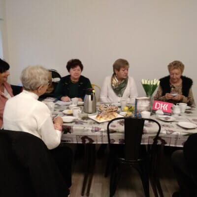 Na zdjęciu widać sylwetki sześciu osób rozmawiających przy stole, a także omawianą książkę, napis DKK i wazon z kwiatami. Kliknięcie w obrazek spowoduje powiększenie.
