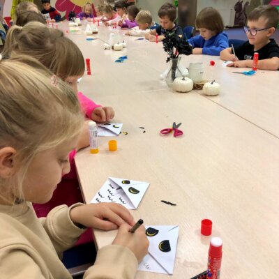 Dzieci siedząc przy stole, tworzą zakładkę metodą origami.