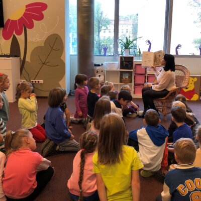 Przedszkolaki uważnie słuchają książki czytanej przez Panią Bibliotekarkę.