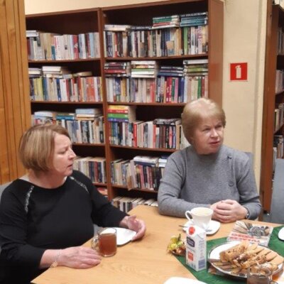 Dwie kobiety siedząc przy stole dyskutują. Za nimi widoczne regały z książkami. Kliknięcie w zdjęcie spowoduje powiększenie.