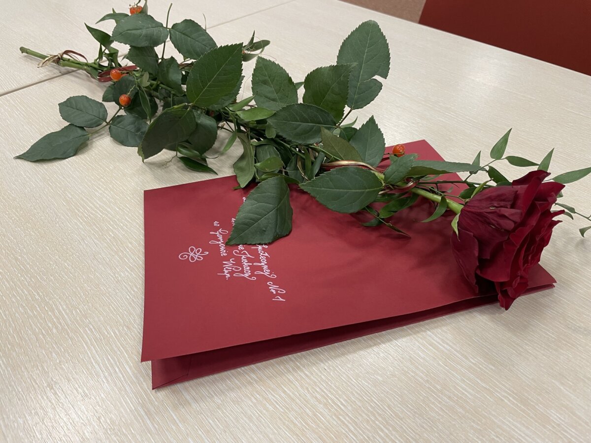 Zdjęcie ozdobnej teczki w kolorze czerwonym, na niej leży róża