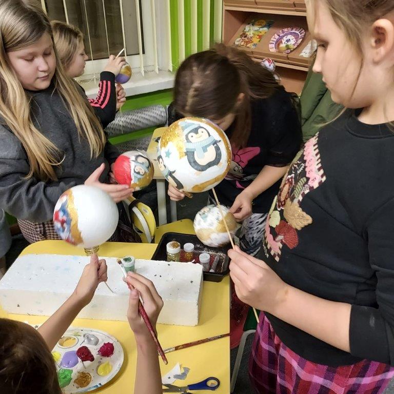 Dzieci w wieku szkolnym wykonują bombki choinkowe techniką zdobienia decoupage ze styropianowych kul, malują je farbami i ozdabiają brokatem