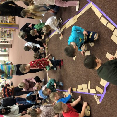 Dzieci układają cegły z kartonu wewnątrz wyklejonego taśmą domku. Kliknięcie w obrazek spowoduje powiększenie.
