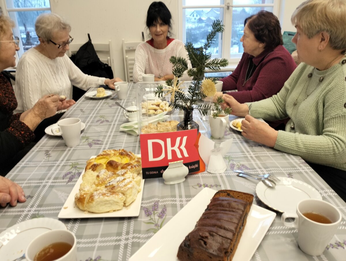 Pięć pań siedzi przy stole i rozmawia. Na środku stołu widnieje naklejka z napisem DKK.