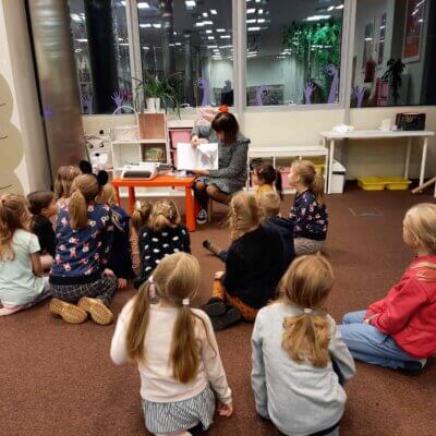 Dzieci siedzą na dywanie i w skupieniu oglądają ilustracje w książce prezentowanej przez Panią Bibliotekarkę. Kliknięcie w obrazek spowoduje powiększenie.