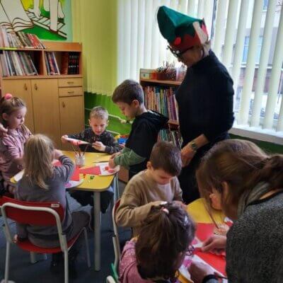 Dzieci siedzące przy stolikach wykonują przy pomocy nauczycielki i Pani Mirosławy Winnickiej Mikołaje z papierowych talerzyków i kolorowego papieru. Kliknięcie obrazka spowoduje powiększenie.