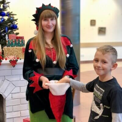 Pani Elf częstuje chłopca cukierkami z mikołajkowej czapki. Kliknięcie w obrazek spowoduje powiększenie.