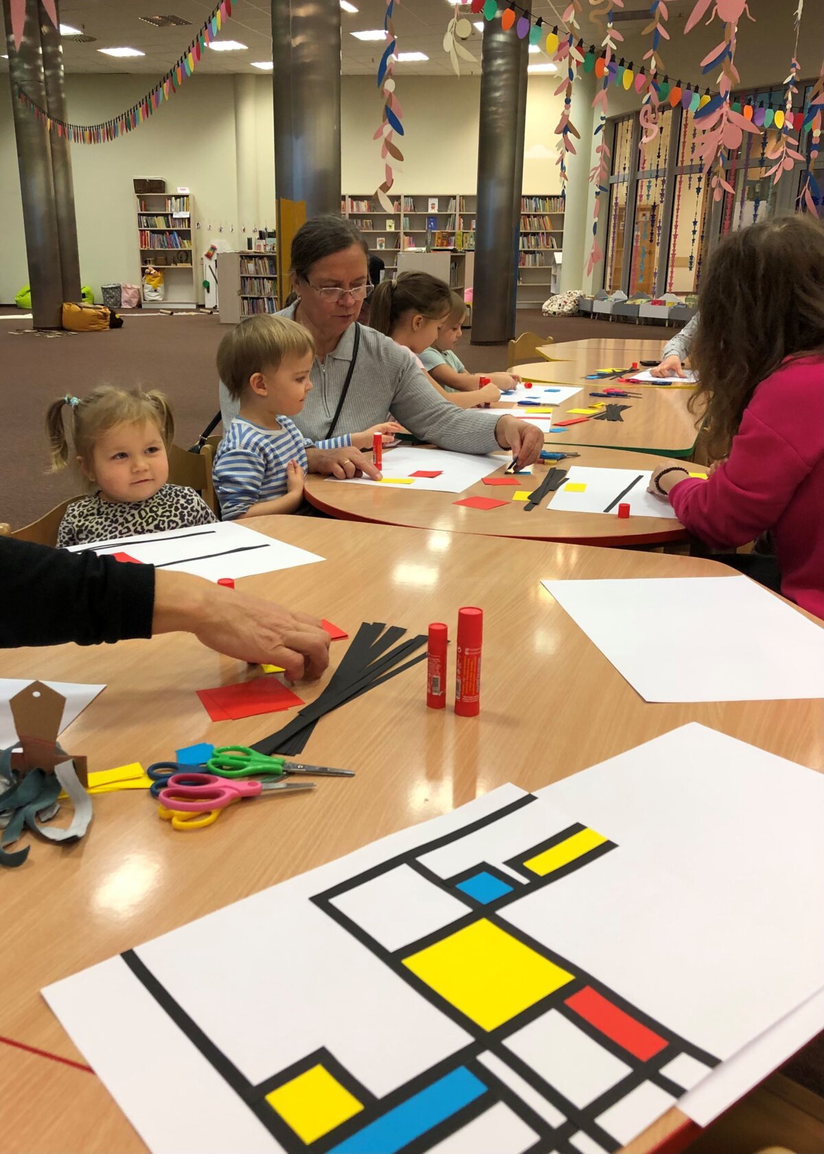 Dzieci wraz z opiekunami wykonują abstrakcyjne obrazki na wzór twórczości Pieta Mondriana.