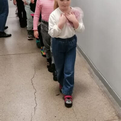Dzieci idące gęsiego po nitce z woreczkami na głowach w długim szarym korytarzu. Kliknięcie spowoduje powiększenie zdjęcia.