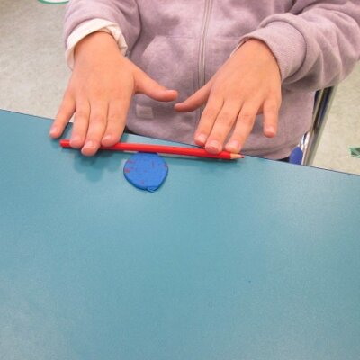 Dziewczynka gniotąca czerwona kredką plastelinę na niebieskim stole. Kliknięcie powoduje powiększenie zdjęcia.