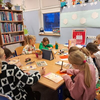 Dzieci siedzą przy stole i wypełniają Dzienniczki DKK. Kliknięcie powoduje powiększenie zdjęcia.