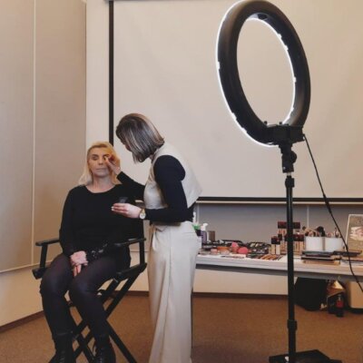 pokaz makijażu - instruktorka nakłada makijaż modelce siedzącej na krześle. Kliknięcie powoduje powiększenie zdjęcia.