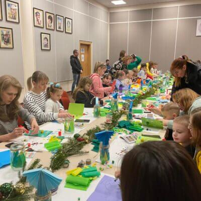 Warsztaty tworzenia ozdób świątecznych dla dzieci. Dzieci wykonują ozdoby świąteczne przy stole. Kliknięcie w zdjęcie spowoduje powiększenie.