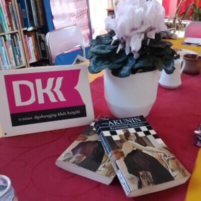 Na stole obok doniczki z kwiatami leża dwie książki i nais DKK