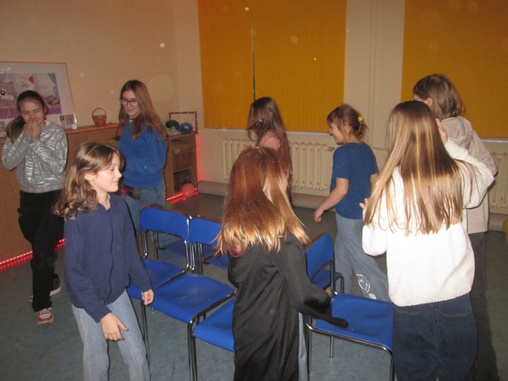 Grupa roześmianych dziewczynek tańczy wokół krzeseł na środku pomieszczenia. Klikniecie powoduje powiększenie zdjęcia.