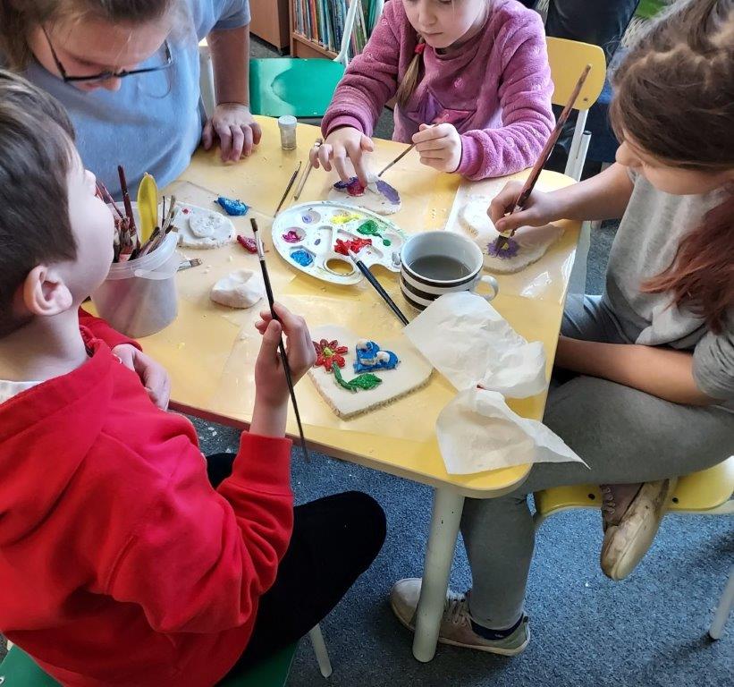 Dzieci siedzące przy stoliku malują farbami serca wykonane z masy solnej