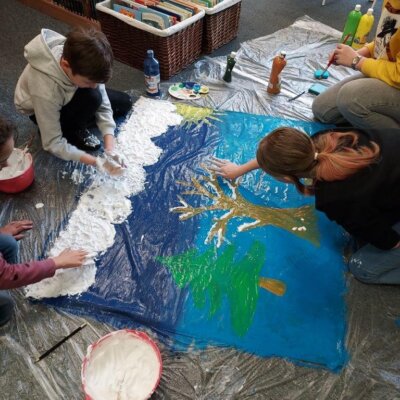Dzieci wspólnie na dużej kartce malują zimowy krajobraz farbami plakatowymi oraz farbą wykonaną z pianki do golenia. Klikniecie powoduje powiększenie zdjęcia.