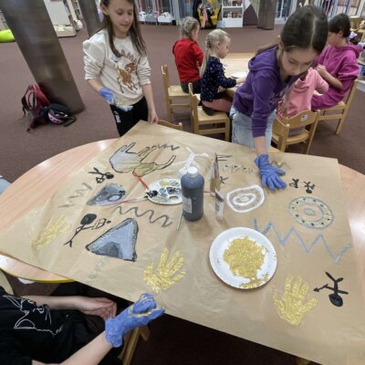 Dziewczynki odbijają dłonie, na papierze tworząc „skalne malowidła”. Kliknięcie powoduje powiększenie zdjęcia.