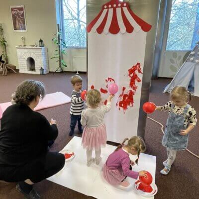 Dzieci malują balonami na czerwono po brystolu naklejonym na biblioteczne słupy. Kliknięcie w zdjęcie spowoduje powiększenie.