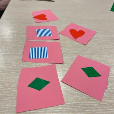 Karty do gry w kolorze różowym z elementami zielonymi, biało-niebieskimi i czerwonymi. Kliknięcie powoduje powiększenie zdjęcia.
