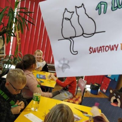 Dzieci przy stolikach wycinają koty z papieru. Kliknięcie powoduje powiększenie zdjęcia.