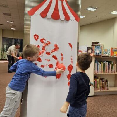 Chłopcy dekorują czerwonymi farbami cyrk przy pomocy balonów. Kliknięcie w obrazek spowoduje powiększenie.