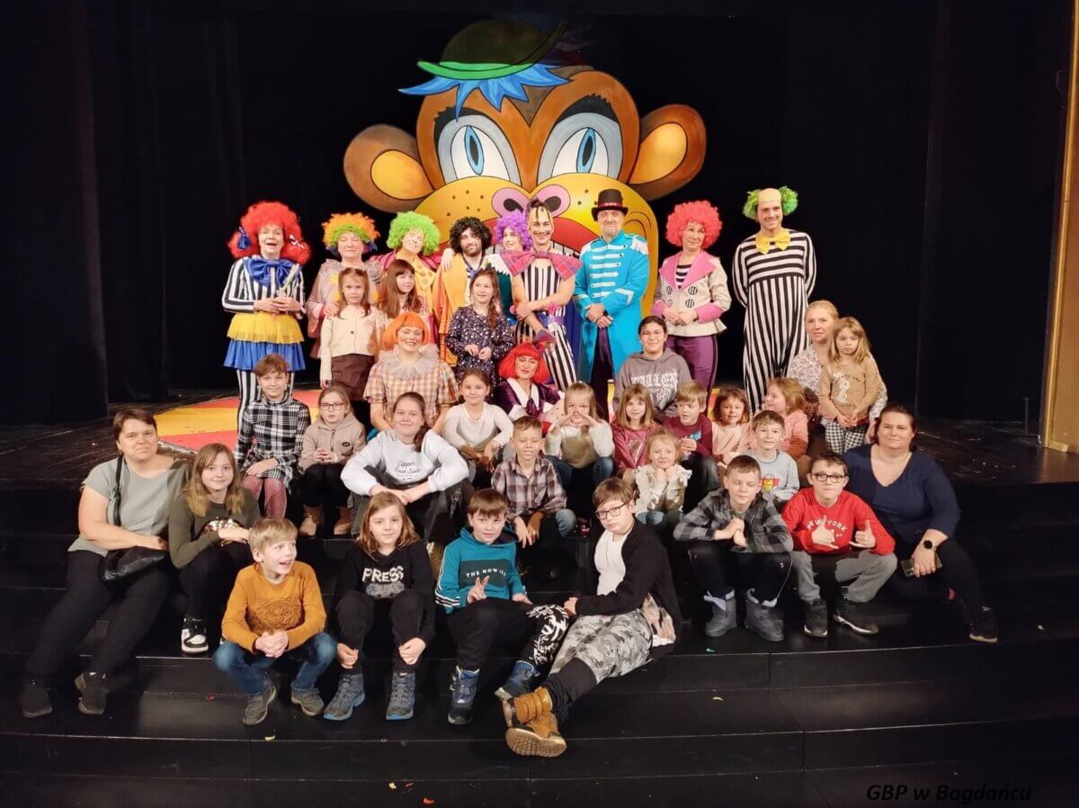 Grupa dzieci z opiekunkami i aktorami na scenie teatru.