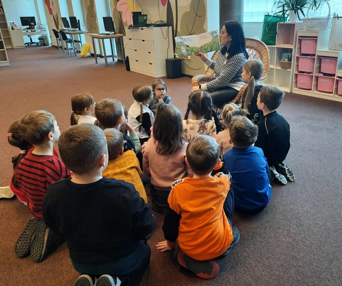 Przedszkolaki w skupieniu słuchają książki czytanej przez Panią Bibliotekarkę.