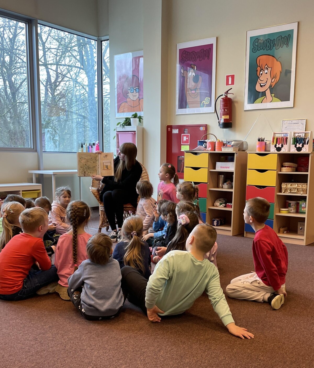 Przedszkolaki słuchają książki czytanej przez Panią Bibliotekarkę.