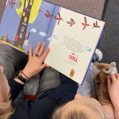 Bibliotekarka czyta dzieciom książkę i pokazuje ilustracje. Obok siedzi dziewczynka i ma pacynkę lisa na ręce. Kliknięcie powoduje powiększenie zdjęcia.