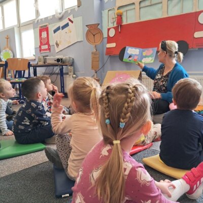 Dzieci siedzą na dywanie, bibliotekarka czytam im książkę o Śwince Peppie. Kliknięcie w obrazek spowoduje powiększenie.
