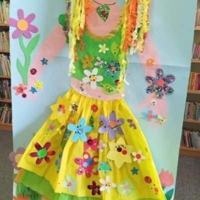 Postać Pani Wiosny, wykonana za pomocą farb i bibuły na dużej, przypiętej do regału kartce, ozdobiona zrobionymi przez dzieci kolorowymi, papierowymi kwiatami. Kliknięcie powoduje powiększenie zdjęcia.