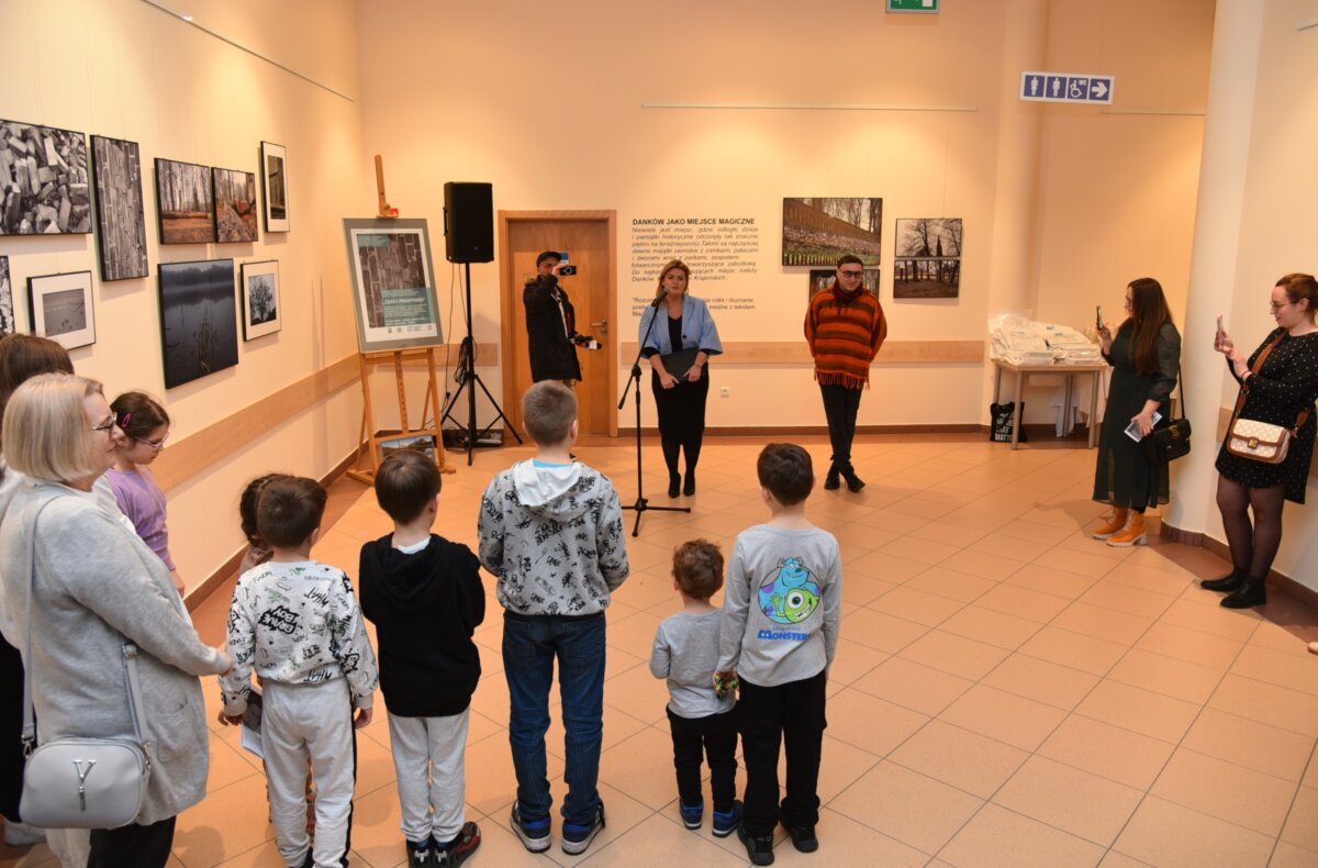 Wnętrze biblioteki. Na pierwszym planie uczestnicy spotkania, przy mikrofonie prowadząca spotkanie.