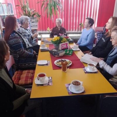 Siedem kobiet siedzi przy stole, na stole filiżanki z herbatą, kwiaty i książki, trwa potkanie DKK. Kliknięcie powoduje powiększenie zdjęcia.