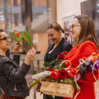 Na zdjęciu autorki uśmiechają się, trzymają dużo kwiatów i przyjmują tulipany od jednej z uczestniczek wydarzenia. Kliknięcie powoduje powiększenie zdjęcia.