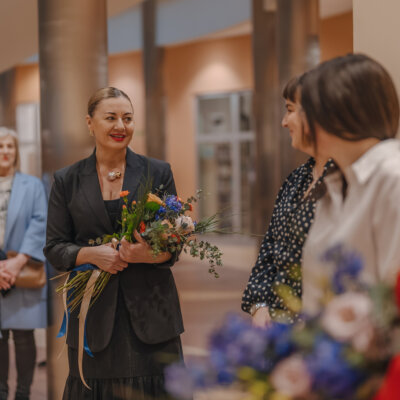 Na zdjęciu jedna z autorek trzyma kwiaty i przemawia do organizatorek wystawy. Kliknięcie powoduje powiększenie zdjęcia.