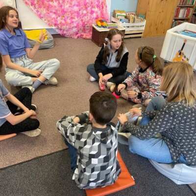 Dzieci wraz z bibliotekarką siedzą na dywanie i rozmawiają o omawianej książce. Kliknięcie w obrazek spowoduje powiększenie.